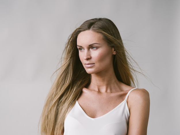 Piękna kobieta naturalny portret dziewczyny z długimi blond włosami na białej szarej ścianie. Strzał studio.