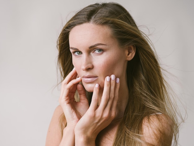 Piękna kobieta naturalny portret dziewczyny z długimi blond włosami na białej szarej ścianie. Strzał studio.