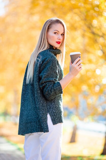 piękna kobieta pije kawę w parku jesienią pod liści jesienią
