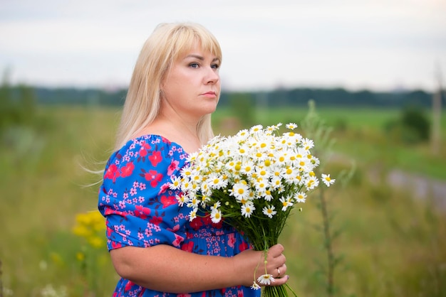 Piękna kobieta plus size z siwymi włosami w letniej sukience pozuje na zewnątrz ze stokrotkami