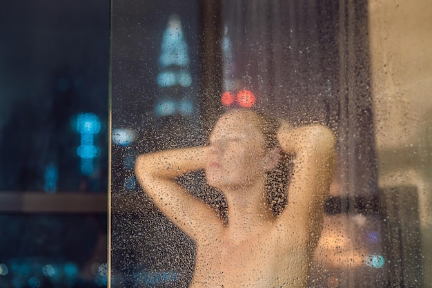 Piękna kobieta pod prysznicem za szybą z kroplami na tle okna z panoramą