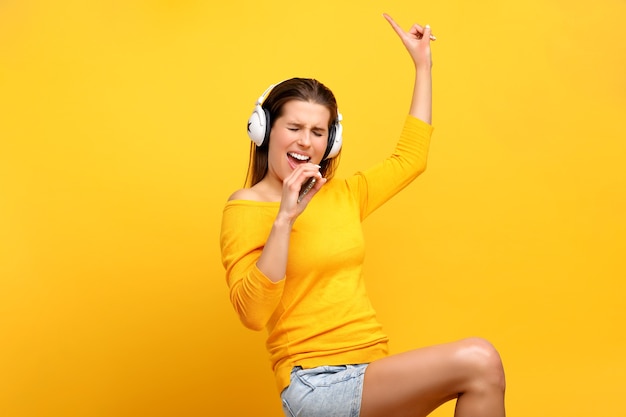 piękna kobieta słucha muzyki na telefonie komórkowym na żółto