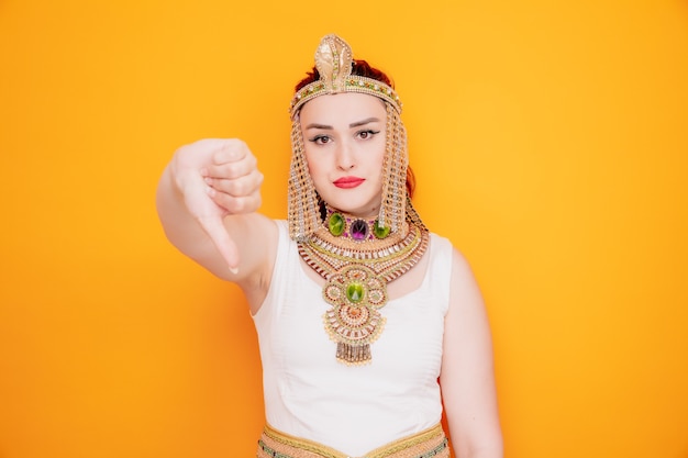 Piękna kobieta, taka jak Kleopatra w starożytnym egipskim stroju, jest niezadowolona pokazując kciuk w dół na pomarańczowo