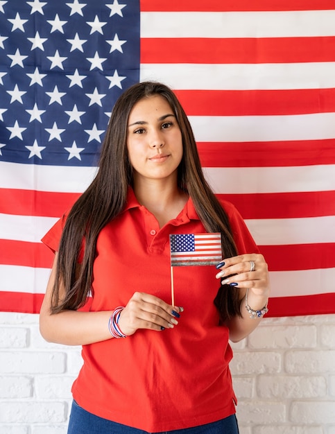 Piękna kobieta trzyma małą flagę narodową na tle flagi USA