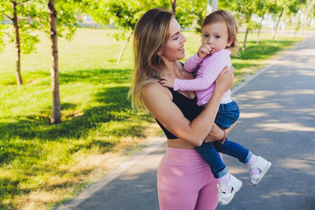 Piękna kobieta trzyma roczne dziecko w ramionach w parku.