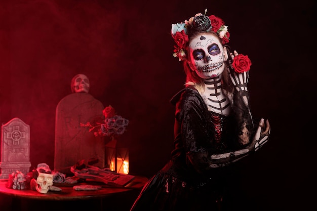 Piękna kobieta trzyma róże na meksykańskie wakacje, wygląda jak santa muerte z kostiumem na halloween i makijażem czaszki. Działając przerażająco i glamour w dniu śmierci zmarłych.