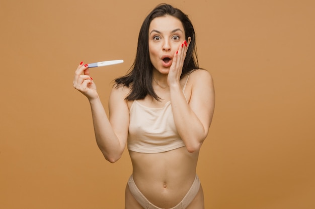Piękna kobieta trzyma test ciążowy z zszokowaną twarzą, młodym i wysportowanym ciałem, pozowanie w bieliźnie
