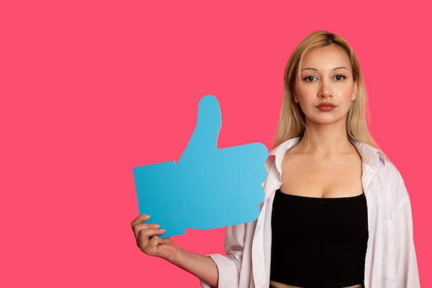 Piękna kobieta trzymająca przycisk "like" na różowym tle