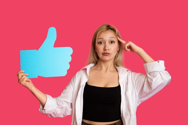 Piękna kobieta trzymająca przycisk "like" na różowym tle