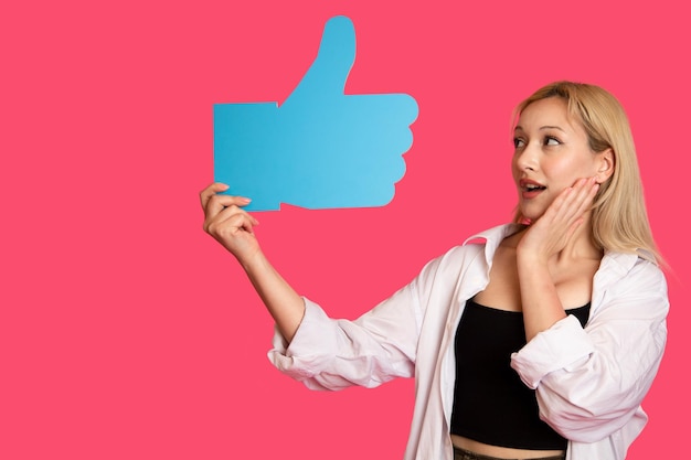 Piękna kobieta trzymająca przycisk "like" na różowym tle