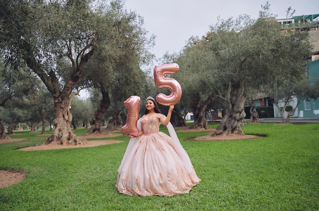 Piękna kobieta ubrana w różowy kostium księżniczki z balonami numer 15 na terenach zielonych