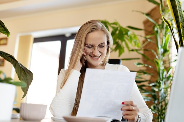 Zdjęcie piękna kobieta uśmiecha się rozmawia przez telefon i czyta dokument praca online biznes online