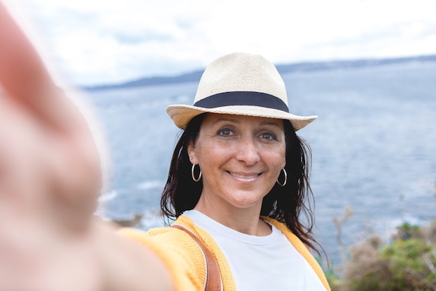 Piękna kobieta uśmiecha się szczęśliwa na zewnątrz w miły dzień w letnim kapeluszu, robiąc zdjęcie selfie