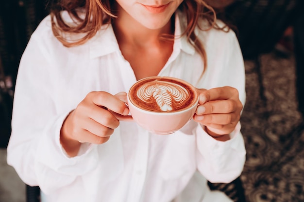 Piękna kobieta w białej koszuli pije cappuccino z latte art w kawiarni