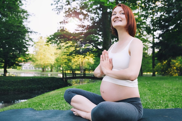 Piękna kobieta w ciąży robi jogę prenatalną na przyrodzie na zewnątrz