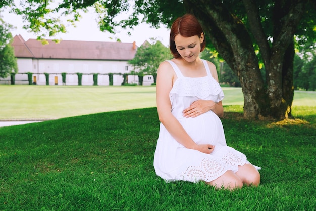 Piękna kobieta w ciąży w białej sukni na naturze na zewnątrz