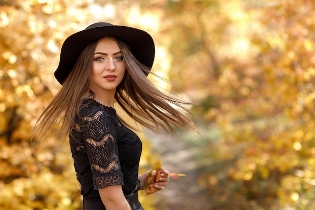 Piękna kobieta w czarnej sukience i kapeluszu jesienią