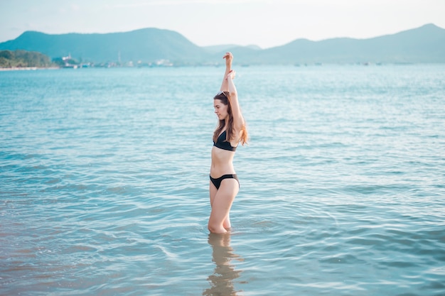 Piękna kobieta w czarnym bikini cieszy się morską wodą na plaży