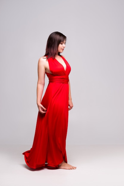 Piękna kobieta w czerwonej sukience na szarej ścianie, portret pełnej długości