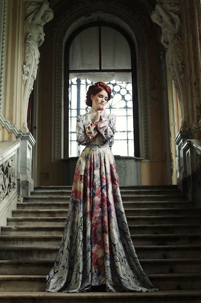 Piękna kobieta w eleganckiej sukni, pozowanie na schodach w starym wnętrzu vintage