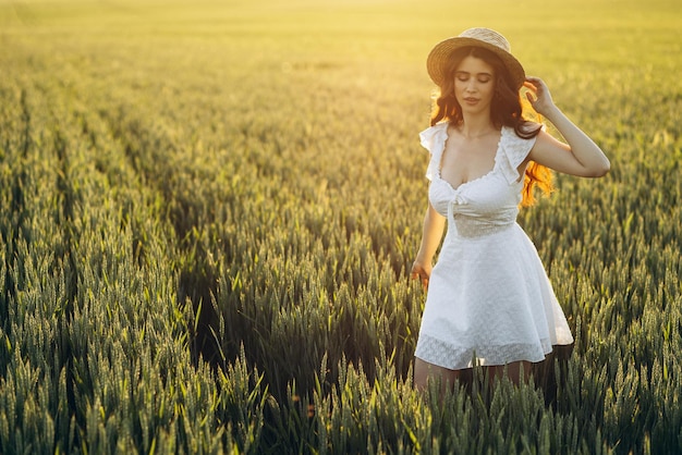 Piękna kobieta w polu ubrana w białą sukienkę i kapelusz