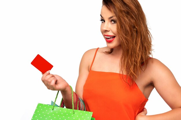 Piękna kobieta w pomarańczowej sukience trzyma w dłoni pustą kartę podarunkową i cieszy się z zakupów