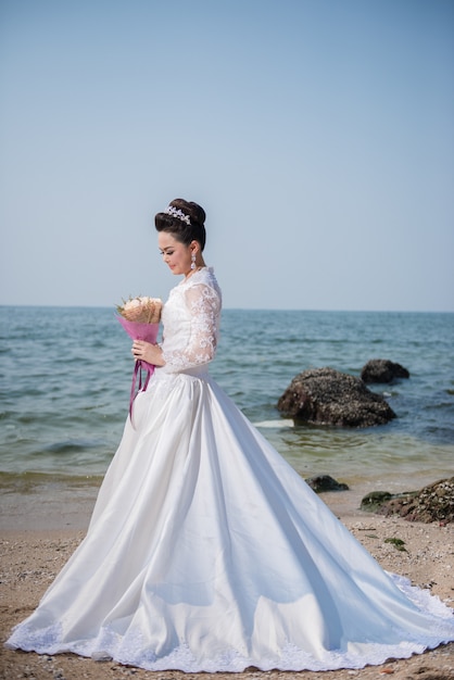 Piękna kobieta w ślubnej sukni mienia kwiatu pozyci na plaży.