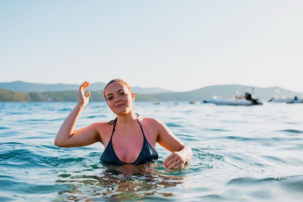 Piękna kobieta w stroju kąpielowym pozuje na morzu o zachodzie słońca