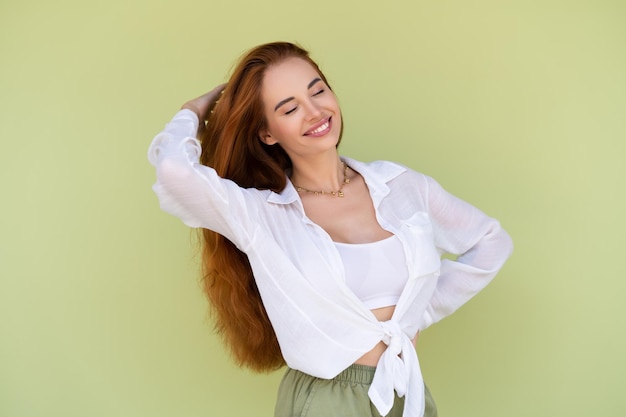 Piękna kobieta z długimi rudymi włosami w swobodnej koszuli na zielonym tle pozytywnie uśmiechnięty śmiejąc się, ciesząc się z wyjścia