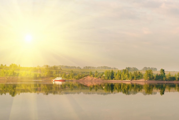 Piękna krajobrazowa plaża z zielonymi drzewami i łodzią na rzece w świetle słonecznym