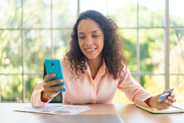 piękna latynoska kobieta używająca smartfona z ręką trzymającą kartę kredytową