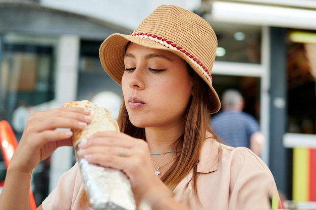 Piękna latynoska kobieta w kapeluszu jedząca kebab w kawiarni w słoneczny dzień
