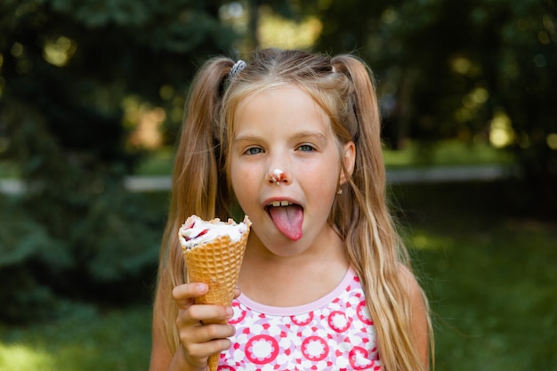 Piękna mała blondynka jedzenie lodów latem w parku. wesoła dziewczyna z lodami.