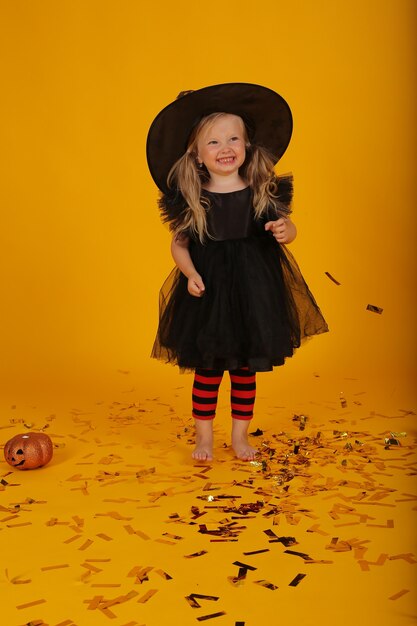 piękna mała blondynka w czarnej sukience i kapeluszu wiedźmy halloween