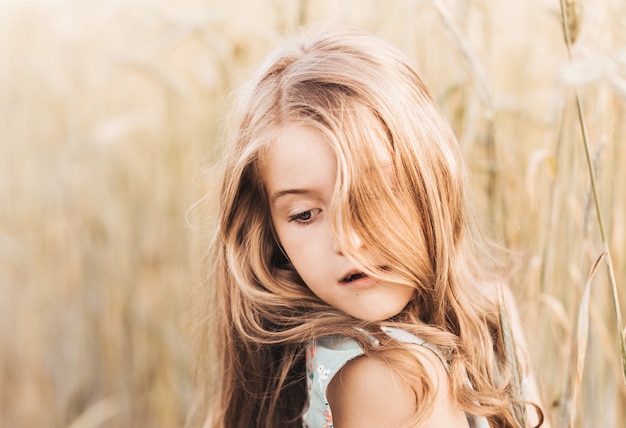 Piękna mała blondynka z długimi włosami spacerująca po polu pszenicy