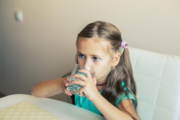 Piękna mała dziewczynka pije czystą wodę z przezroczystego szkła