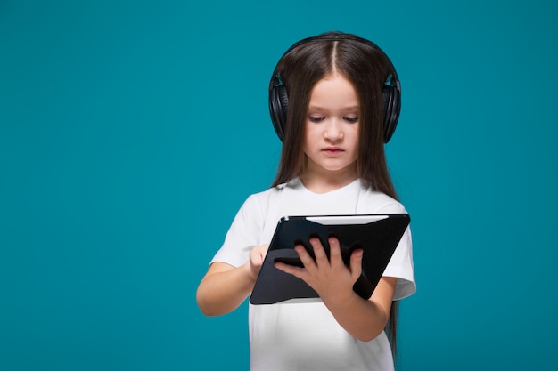 Piękna mała dziewczynka w koszulce i słuchawki z długimi włosami trzymać tablet