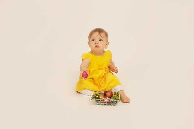 Piękna Mała Dziewczynka W żółtej Sukience Siedzi Obok Małego Kosza Z Warzywami