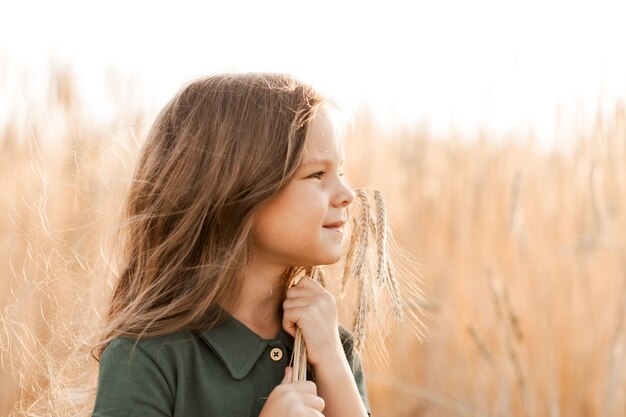 Piękna mała dziewczynka z długimi włosami chodzenie po polu pszenicy w słoneczny dzień. Portret na zewnątrz. Relaks dzieci