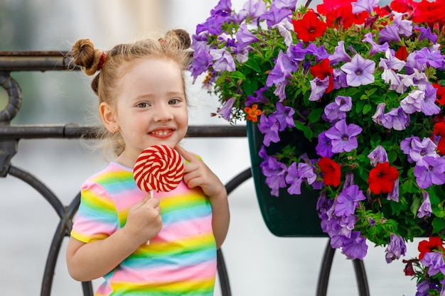 Piękna mała dziewczynka z lizakiem stoi w pobliżu kwiatów