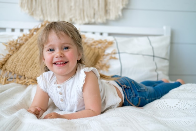 Piękna mała dziewczynka z warkoczami leży na łóżku i śmieje się.