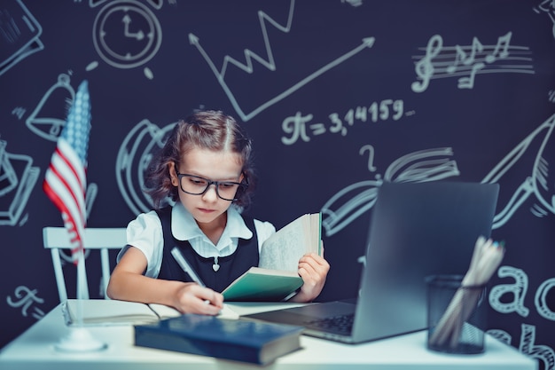 Piękna Mała Uczennica Siedzi Przy Biurku I Uczy Się Online Z Laptopem Na Czarnym Tle Z...