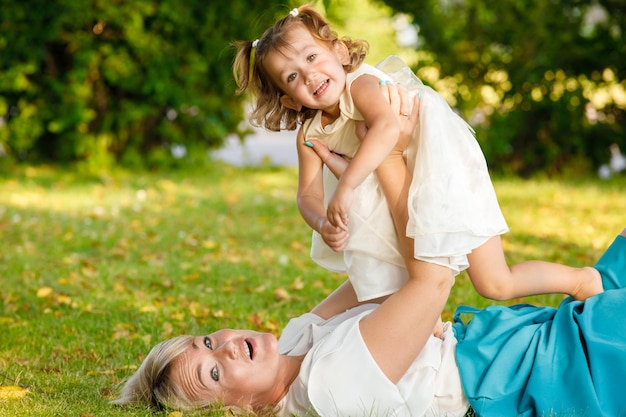 Piękna mama i córka bawią się leżąc na trawie w parku