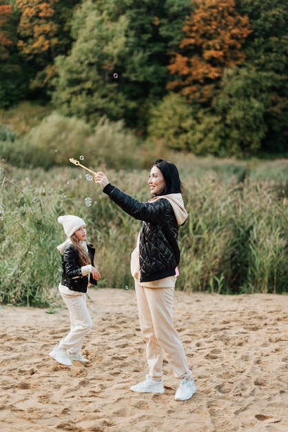 Piękna mama i córka bawią się razem w jesiennym parku na piasku