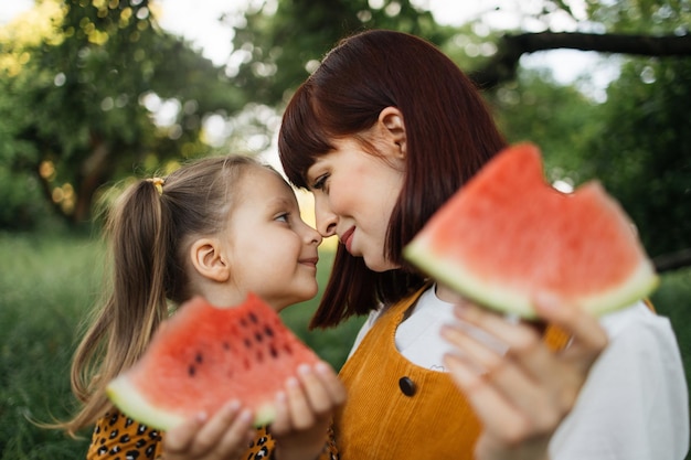 Piękna mama i jej córka trzymają kawałki arbuza podczas odpoczynku na pikniku w parku