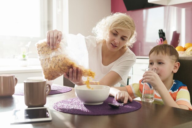 Piękna mama i jej uroczy syn jedzą zdrowe płatki kukurydziane na śniadanie