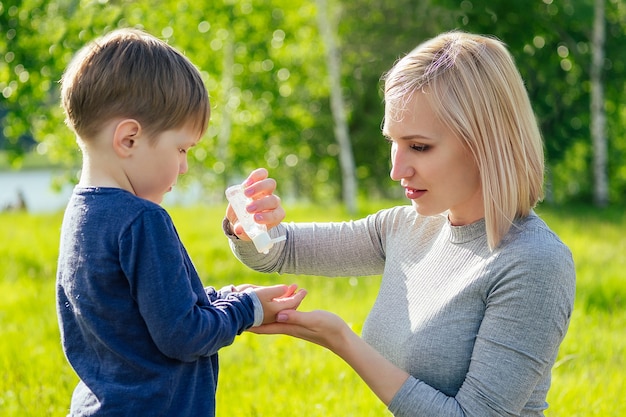 Piękna Mama Nakłada Antyseptyczny żel Na Uroczą Rączkę Syna W Parku Na Tle Zielonej Trawy I Drzew