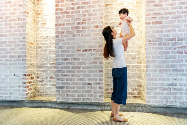 Piękna mama podnosi swoje urocze dziecko w górę i patrzy na nią uśmiechniętą Szczęśliwy rodzic spędzający czas bawiąc się z córką