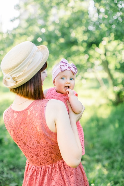 Piękna Mama W Słomkowym Kapeluszu I Jej Córeczka Na Zewnątrz Wyglądają W Różowej Sukience. Plenerowy Portret Szczęśliwa Rodzina. Wygląd Rodziny. Matka I Jej Córka W Lato Parku.