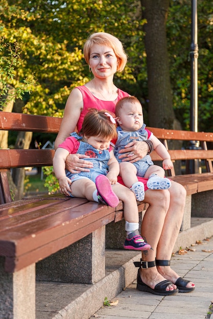 Piękna mama z córką i synem siedzą latem na ławce w parku